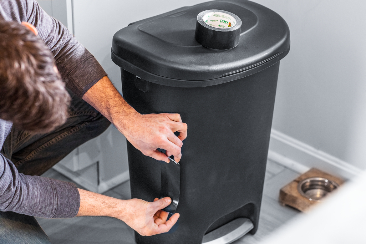 Man fixing crack in garbage can with black duct tape
