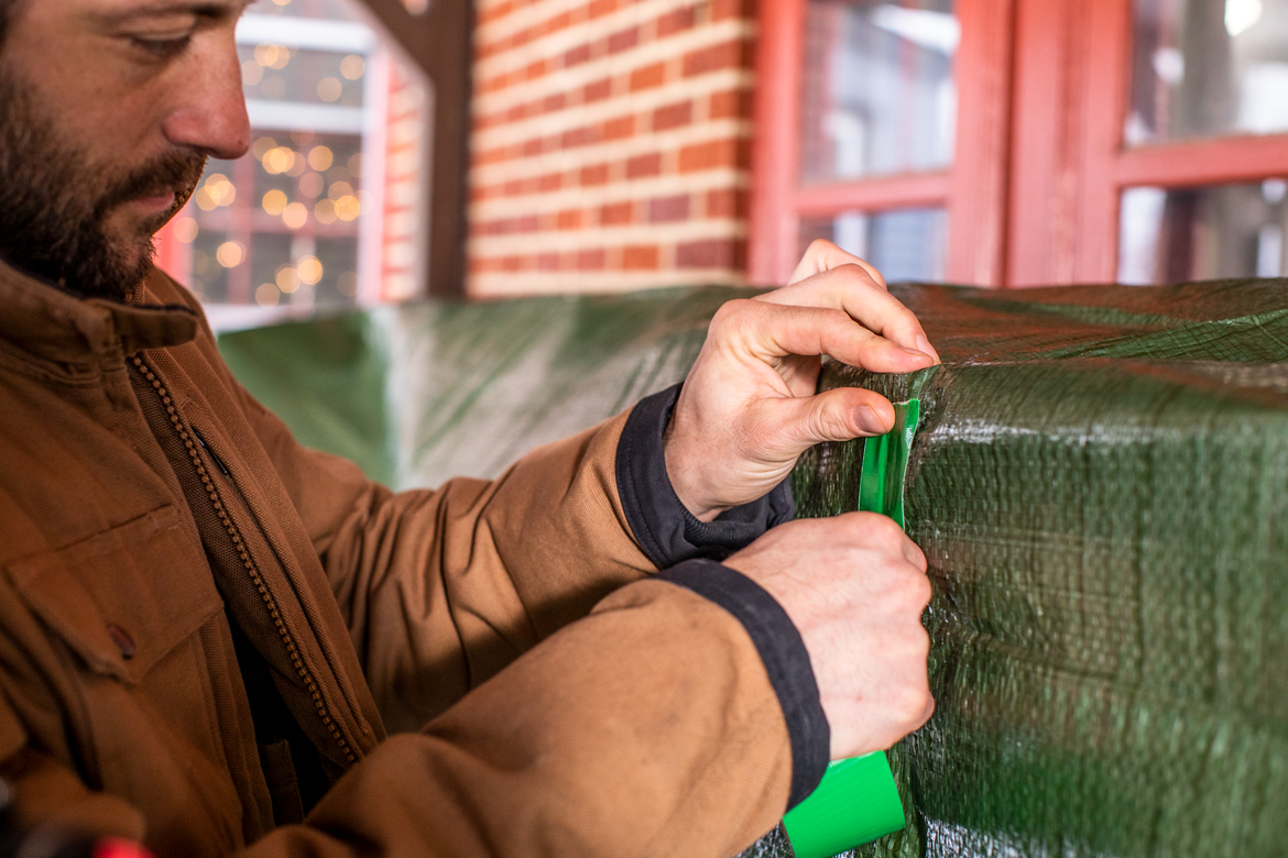 Man repairing green outdoor tarp with green duct tape
