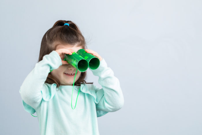 A young girl looking through green duck tape toy binoculars