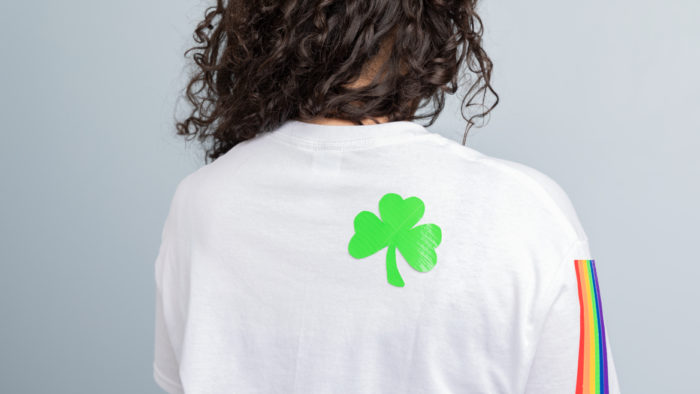 A white shirt with a rainbow sleeve and a green shamrock on it.