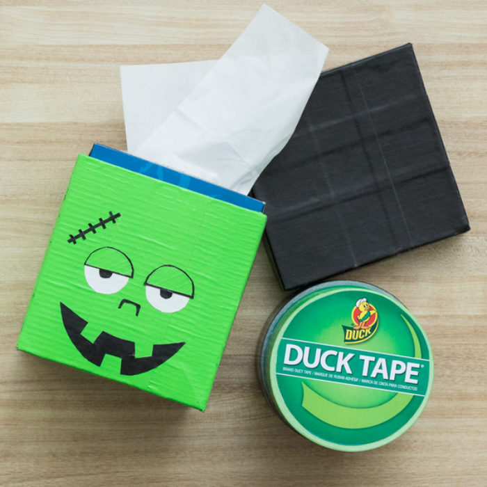 A tissue box covered with green Duck Tape and a monster face.