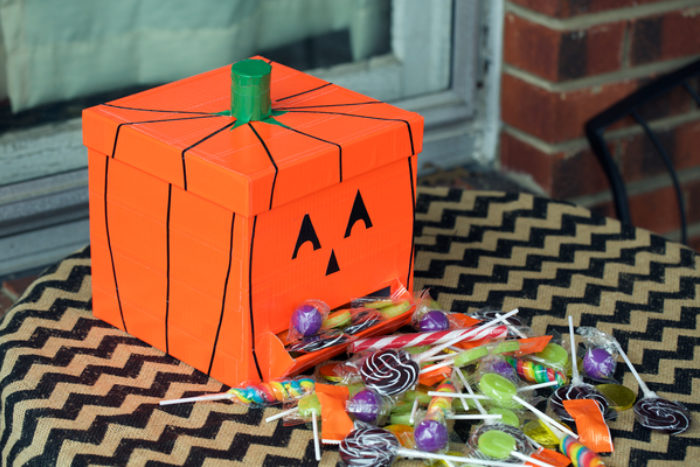 A box decorated as a pumpkin with orange duck tape.