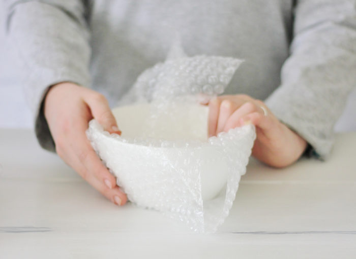 A bowl being wrapped in bubble wrap.