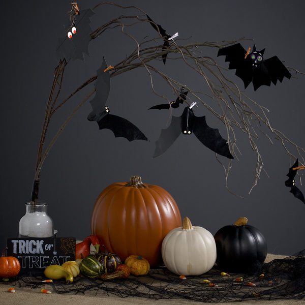 Completed Duck Tape Bat Decorations hanging from a branch, surrounded by Halloween decorations