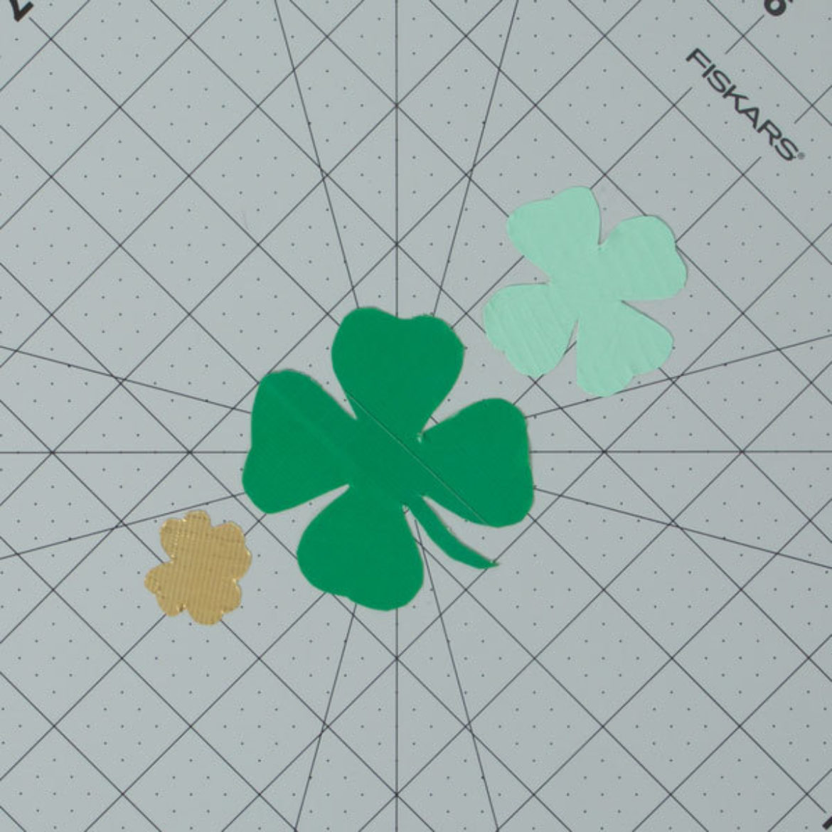 three clover shaped pieces of wax paper covered in different colors of Duck Tape
