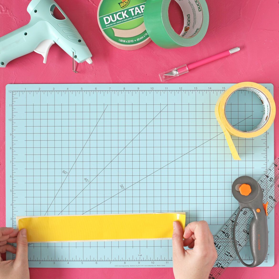 One strip of yellow Duck Tape being laid flat on a crafting board.
