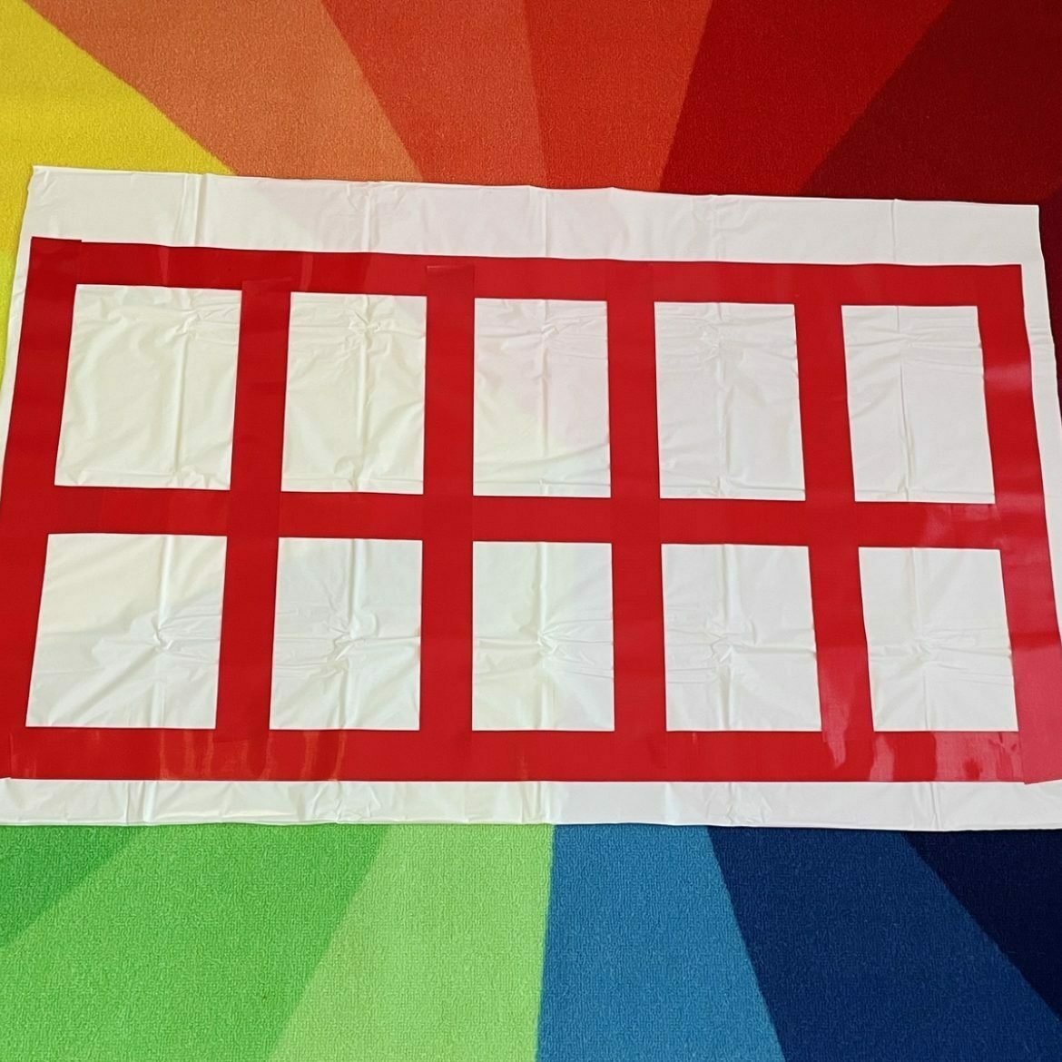 Rectangular white tablecloth with red duct tape squares on a rainbow background for 10 frame