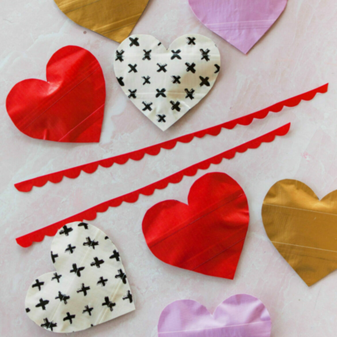 8 duct tape hearts in various colors and prints with a red duct tape garland laid on a white surface