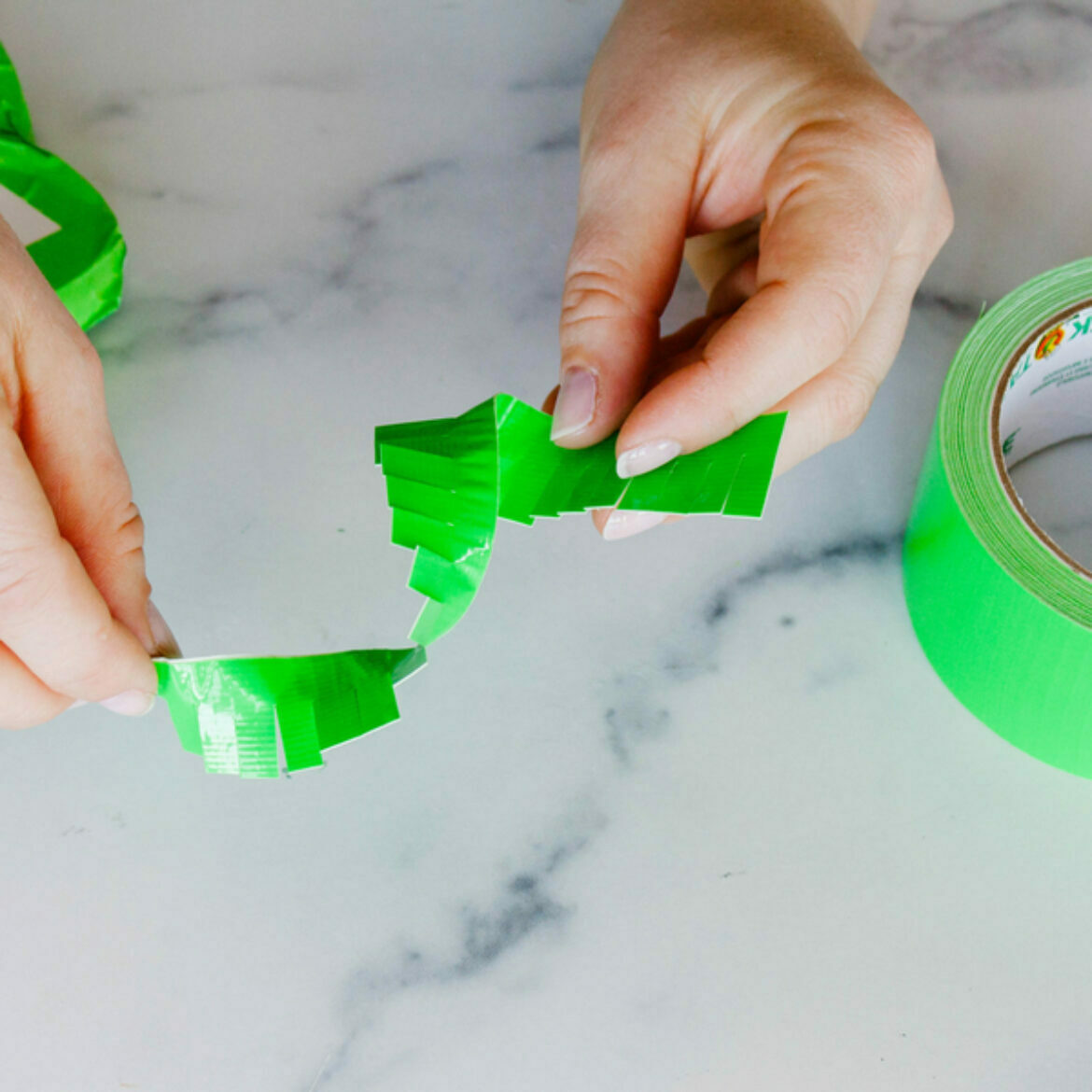 A white marble background with a neon green roll of duct tape and two hand holding fringed duct tape