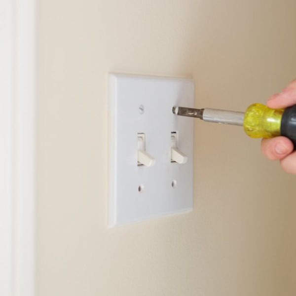 Removing a light switch cover from a wall.